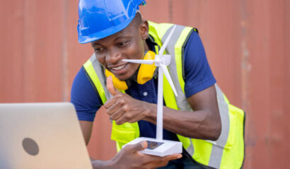 Engineer African American black worker discussing of solar energy from wind turbine model and online with laptop at construction site.