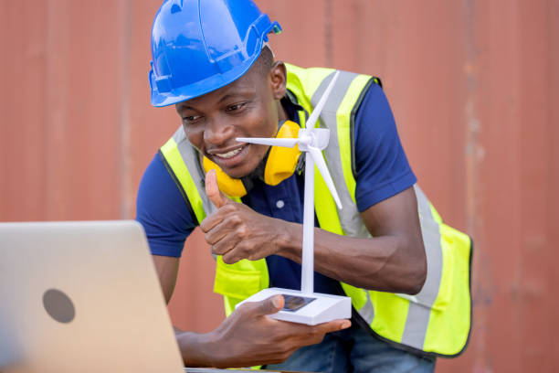 Engineer African American black worker discussing of solar energy from wind turbine model and online with laptop at construction site.