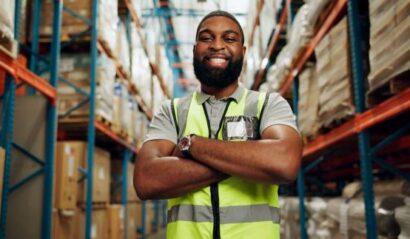 Black man, arms crossed and happy in warehouse on portrait for manufacturing as manager in Uganda. Male person, employee and smile with confidence at wholesale for package, supply chain and delivery
